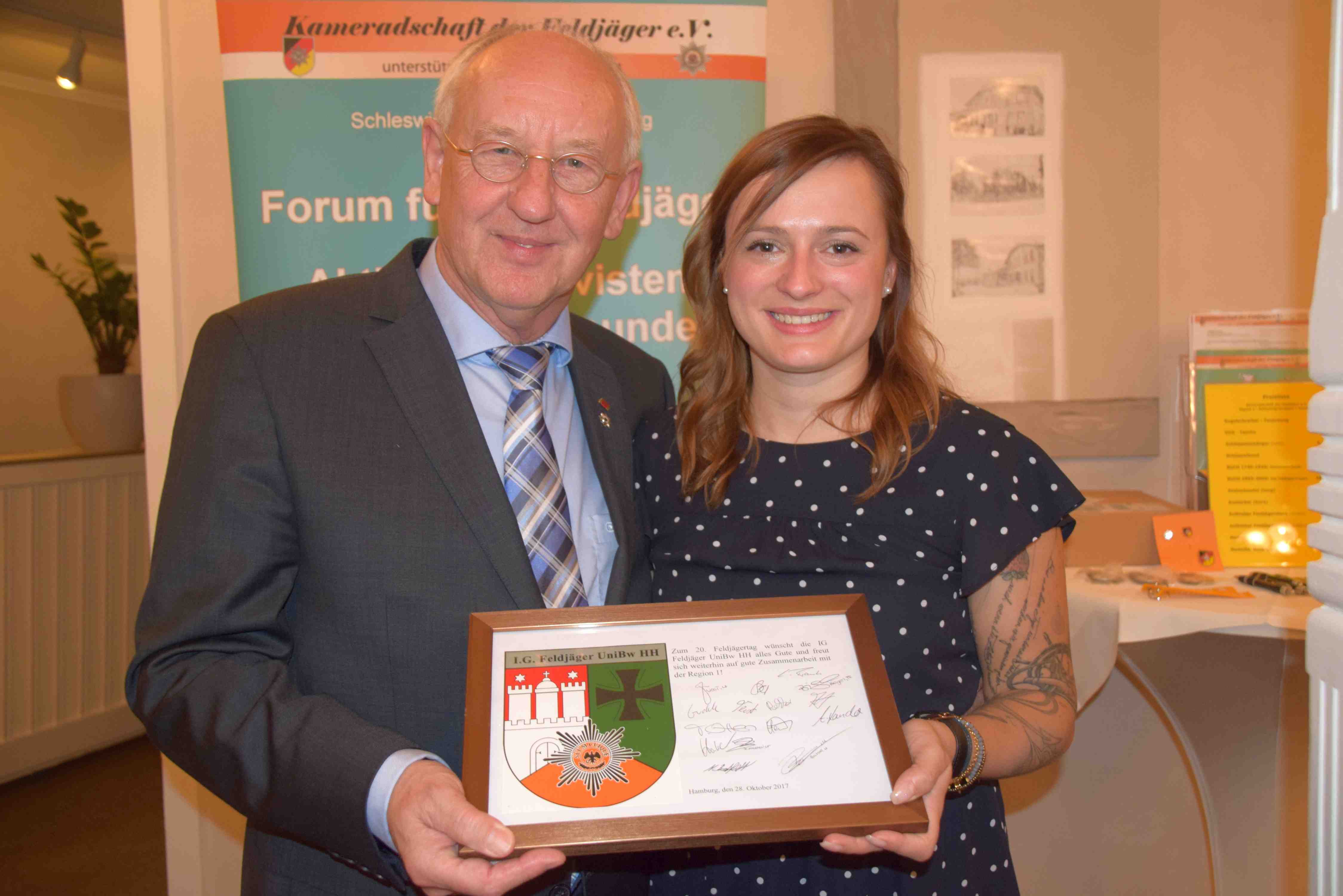 Isabel Biegerl überreicht dem Regionalleiter 1 eine Tafel mit Widmung und neuem Emblem ihrer "Interessengemeinschaft Feldjäger an der UniBw Hamburg"